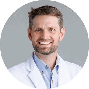 Smiling male doctor in white coat with stethoscope on gray background.